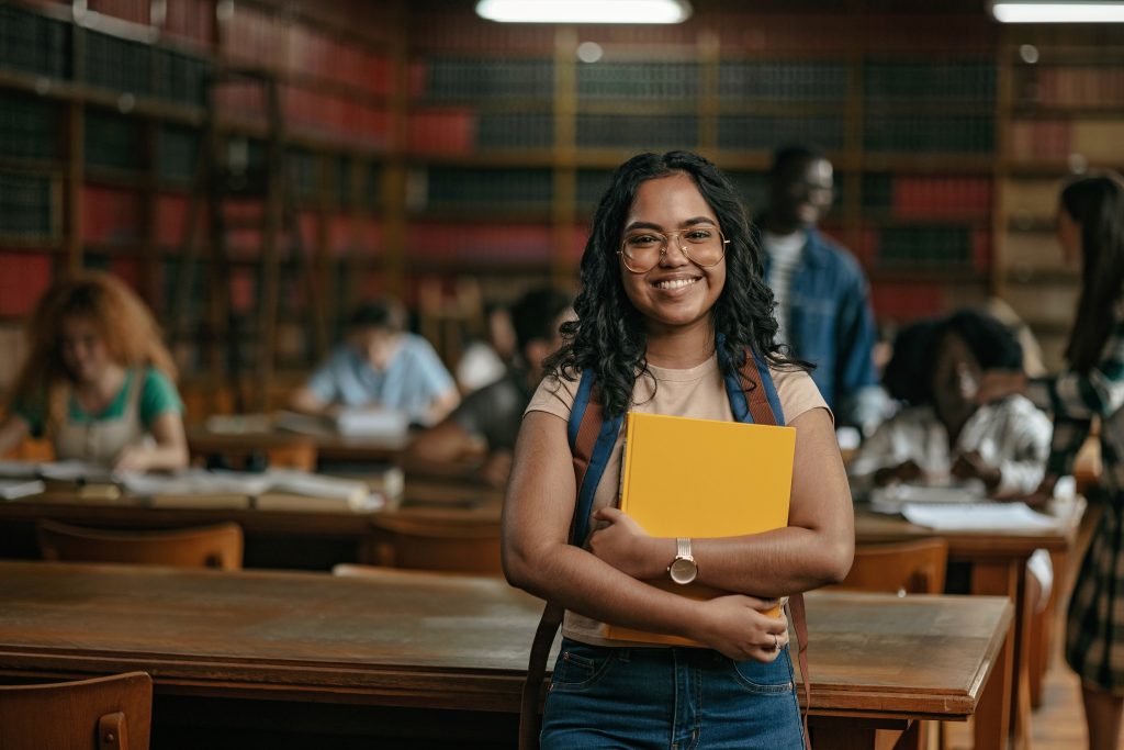 Young adult in classroom with backpack on and notebook