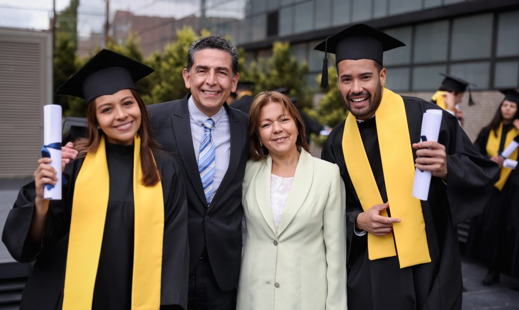 Portrait of happy Latin American graduate students smiling with their parents on their graduation day while looking at the camera - education concepts