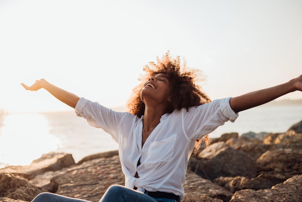 Portrait of a beautiful girl enjoying by the sea with arms outstretched.